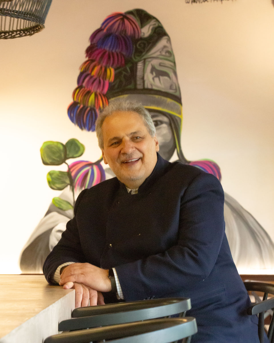 Carlos Renne Cure Lemaitre sonríe junto a una barra de Renne, frente a una obra mural de colores.