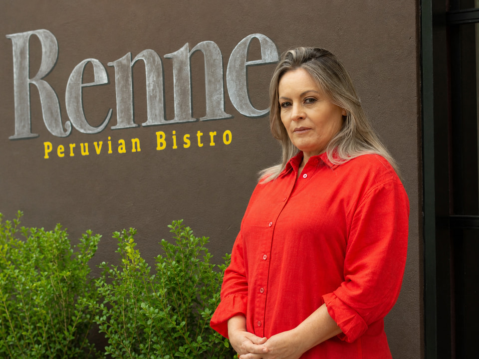 Retrato editorial de Marcela Pulido Muñoz con blusa roja, frente a la pared exterior de Renne Peruvian Bistro.