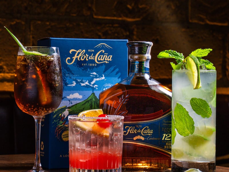 Three cocktails beside a Flor de Caña rum bottle and box in an archival photograph from Renne.